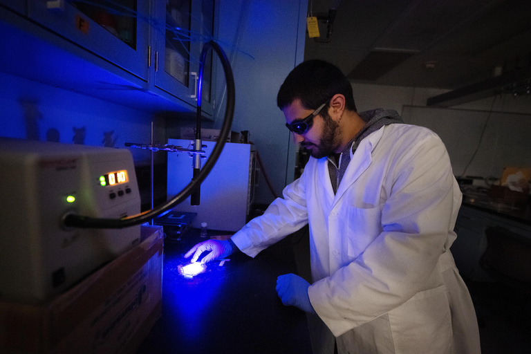 A researcher wearing gloves and eye protection works in the lab
