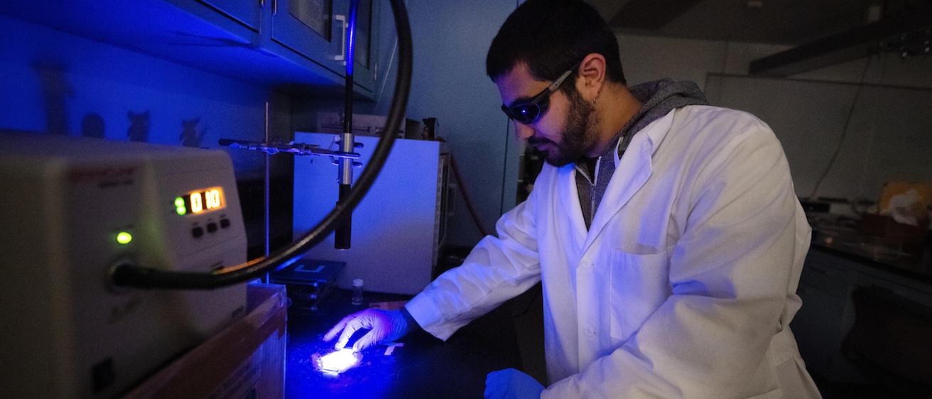 A researcher wearing gloves and eye protection works in the lab